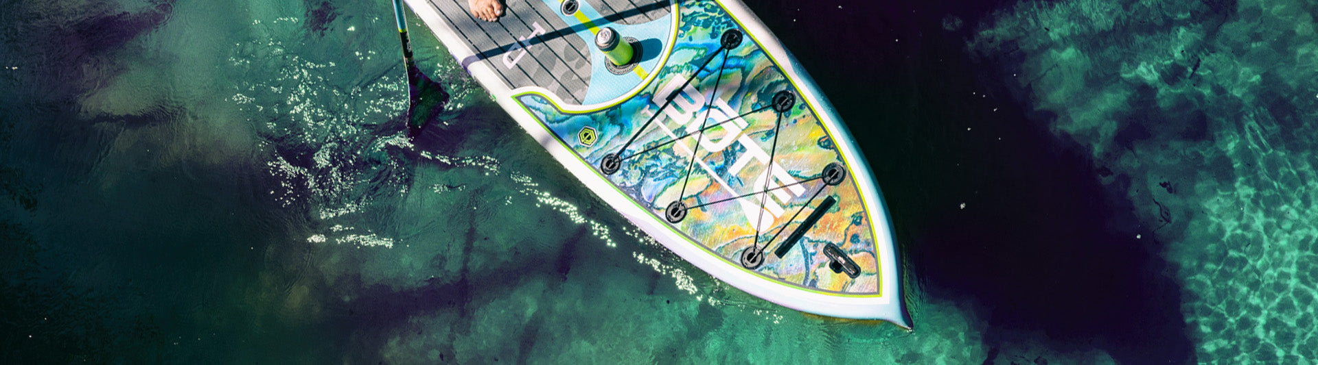 Top view of colorful paddle board floating in clear turquoise water.
