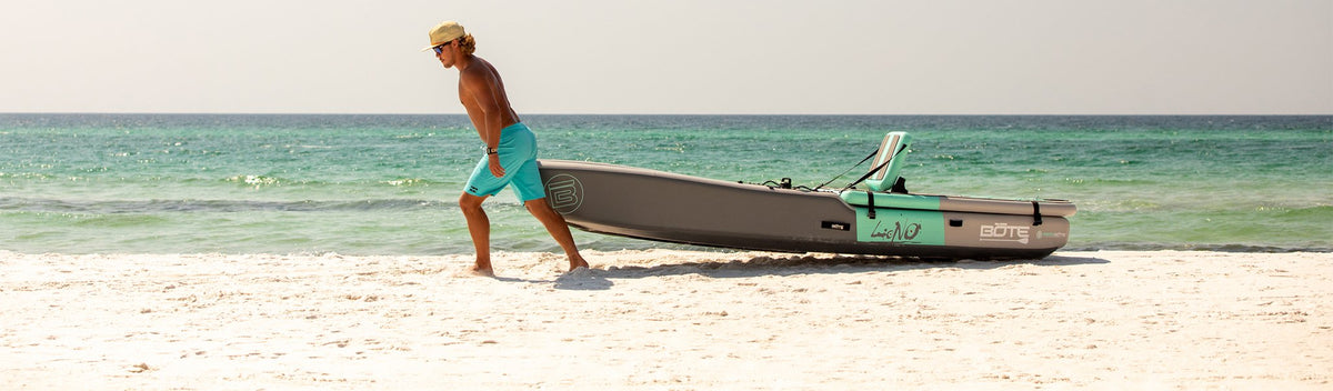 Man pulling kayak onto sandy beach beside turquoise ocean waves.