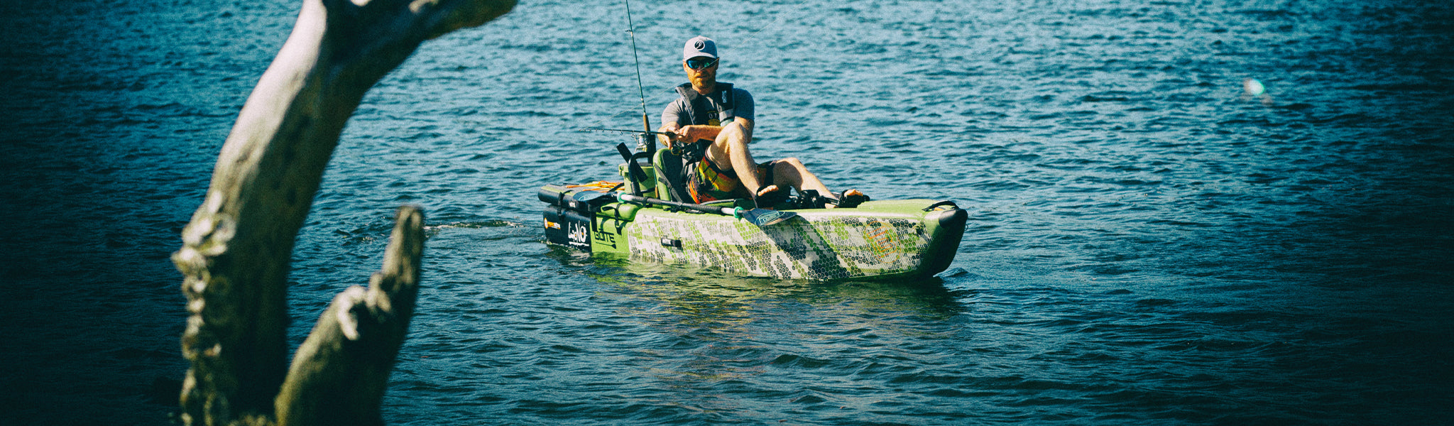 Angler seated in LONO Aero kayak on open water with fishing rod extended near driftwood.
