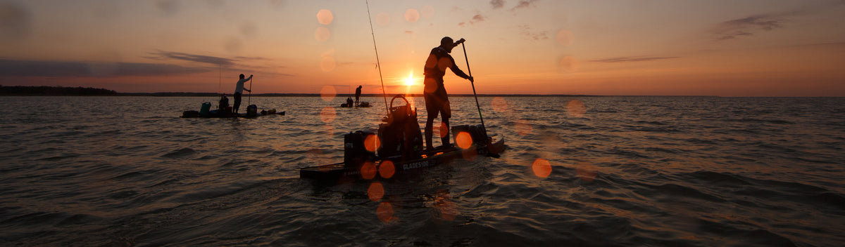 People paddle boarding across calm water at sunset with fishing gear on their boards.
