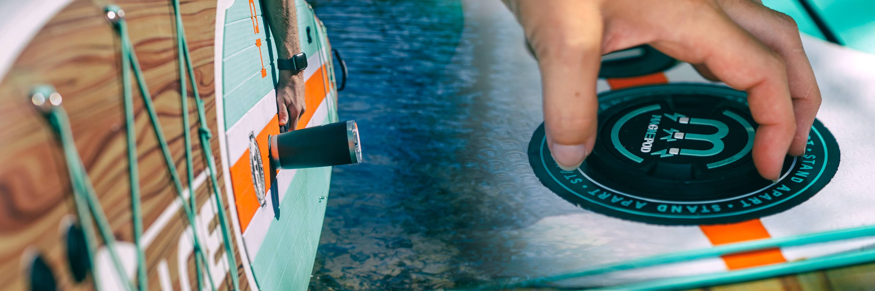 Close-up of paddle board with tumbler attached to MAGNEPOD mount on striped deck.