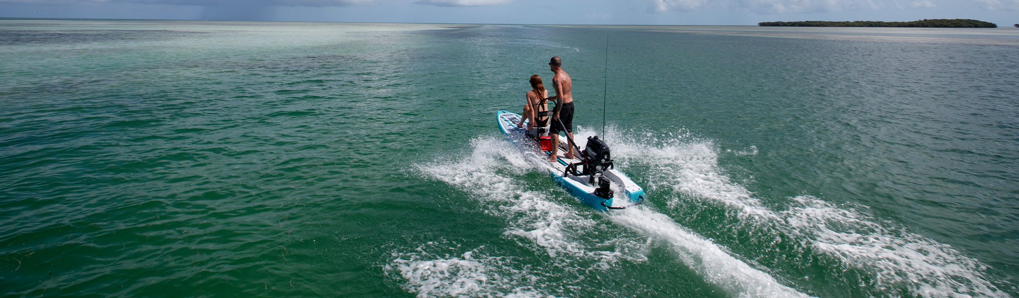 Two people riding motorized paddle skiff across open water on a sunny day.