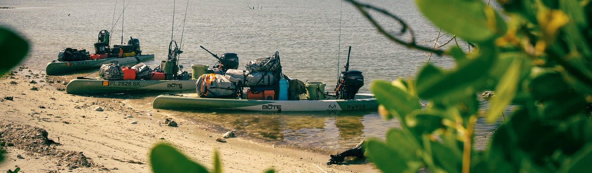 Three loaded paddle skiffs docked on a sandy shore with gear and fishing rods.