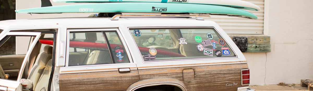 Station wagon covered in stickers with paddle boards strapped to the roof.