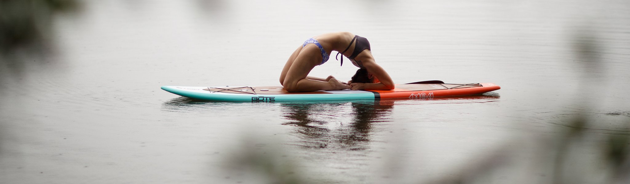 Woman practicing yoga pose on paddle board floating on calm water.