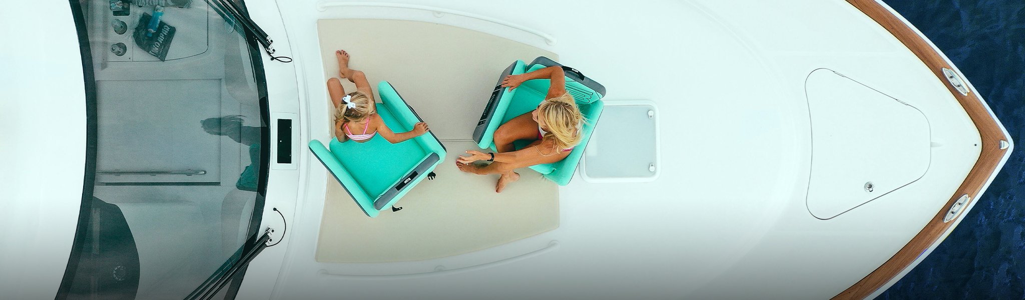 Top view of two women relaxing on teal inflatable chairs on a white boat deck.