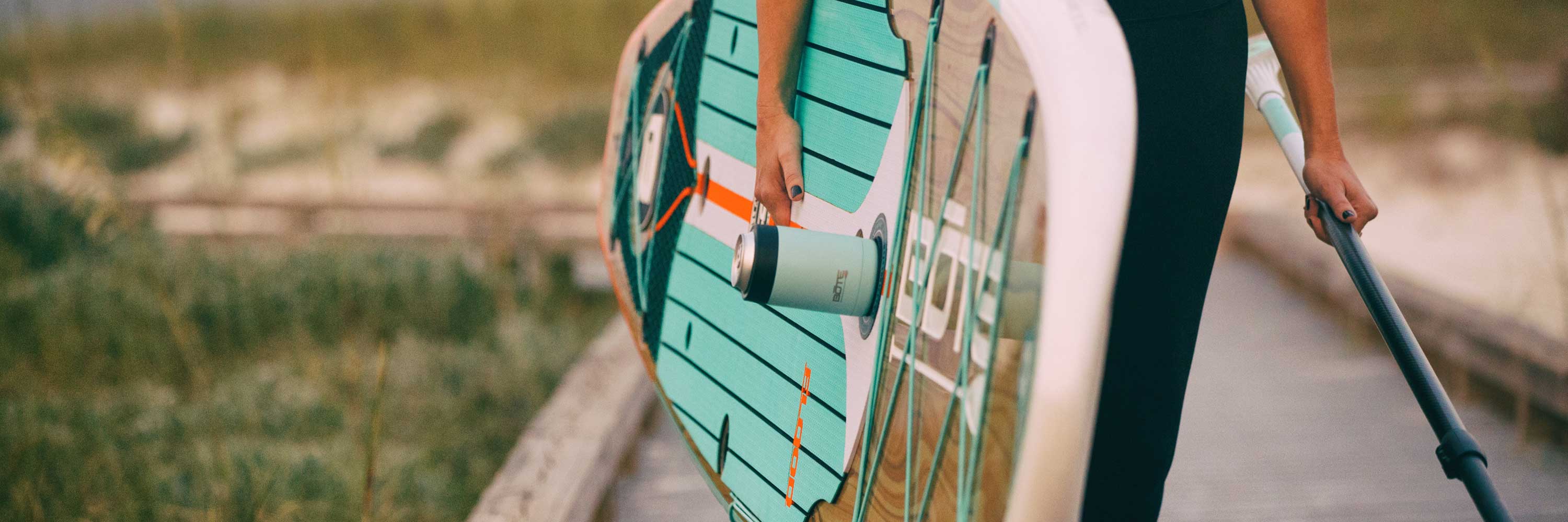 Close-up of person carrying paddle board with tumbler magnetically attached to deck.
