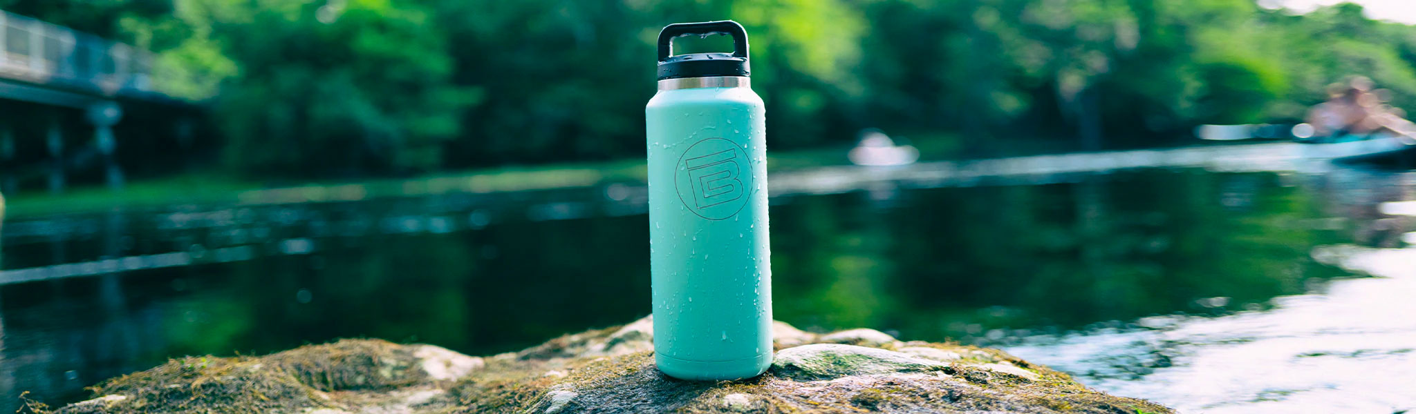 Teal MAGNEBottle with logo sits on a rock beside a calm river.