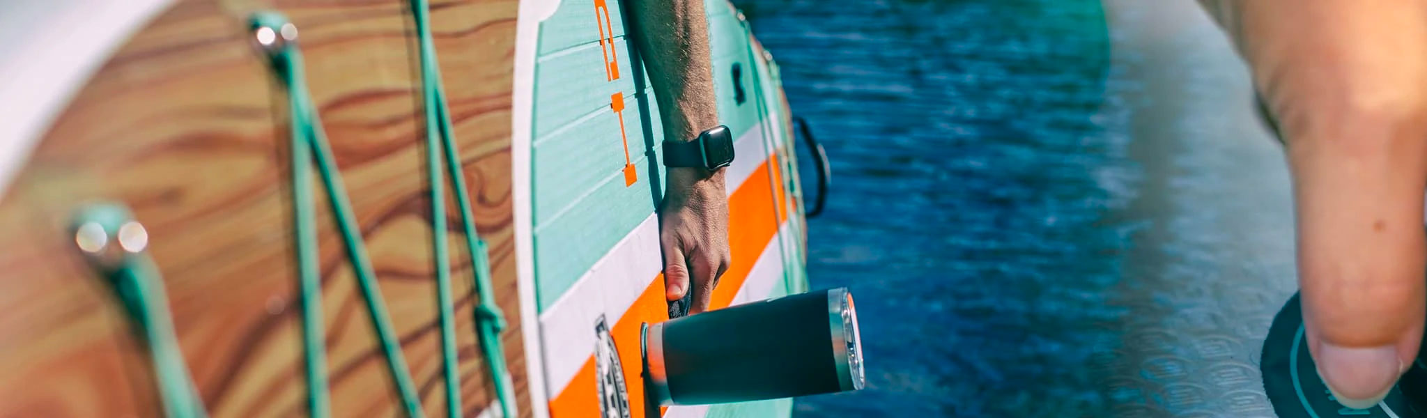 Close-up of hand holding tumbler mounted on paddle board over blue water.