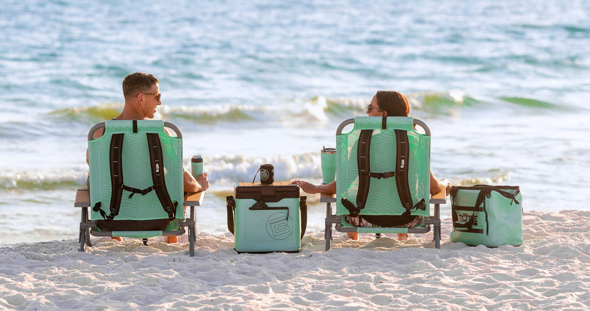 Rear view of two people seated in Mule Dune Chairs on beach with cooler between them.