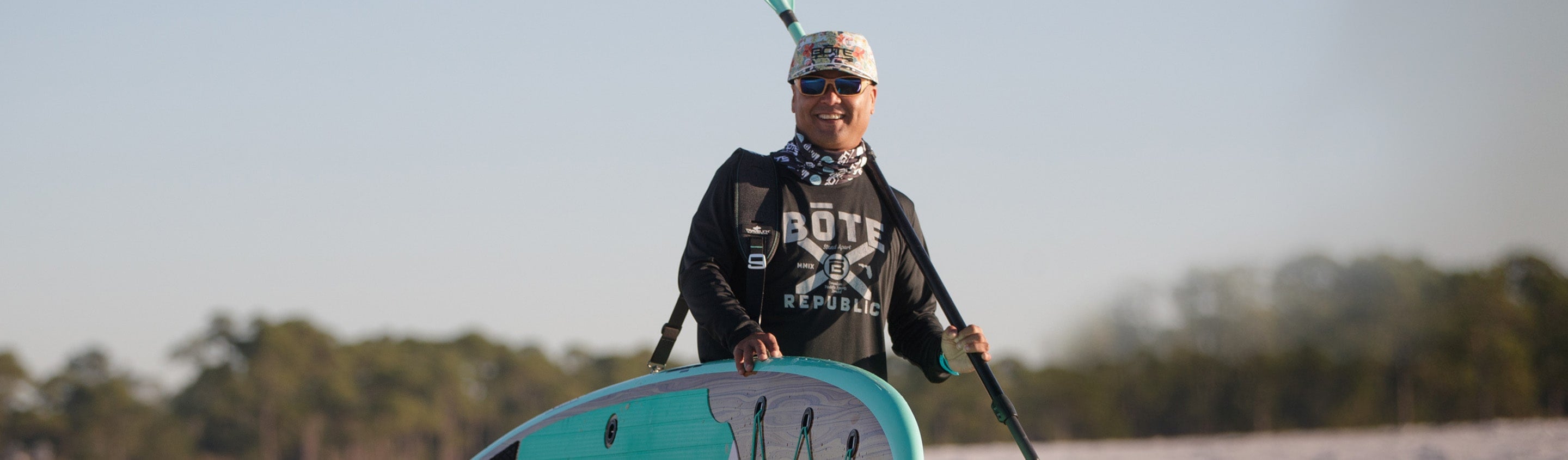 Smiling paddler wearing sun-protective clothing and hat while holding paddle on water.