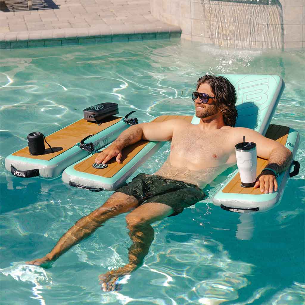 Man lounging on an inflatable chair with cup holders and speakers in a pool.