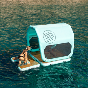 Turquoise inflatable shade tent with gray mesh panels attached to a floating dock with a women climbing up the floating stairs to relax in the shade on the water.