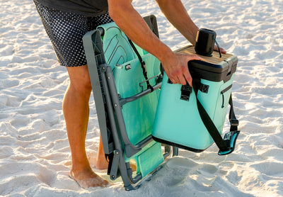 Person attaching KULA Mule cooler to beach chair on sand.