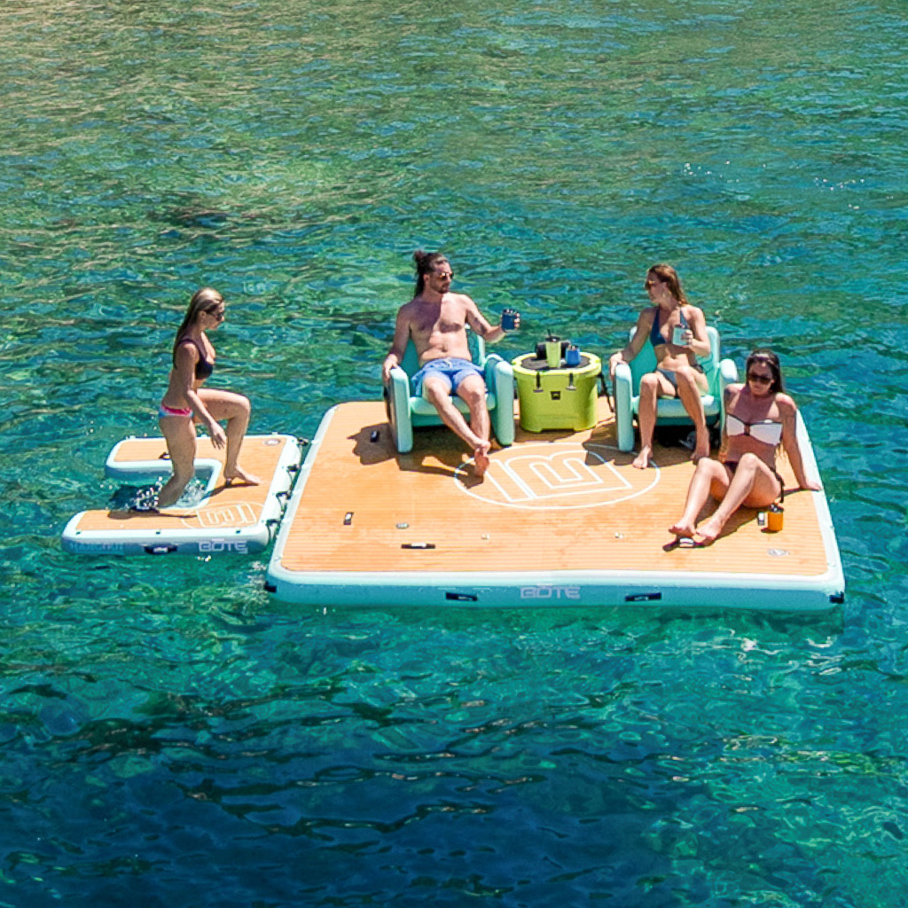 Four people relaxing on an Inflatable Hangout Dock 10 + Ladder Classic floating on clear blue water.