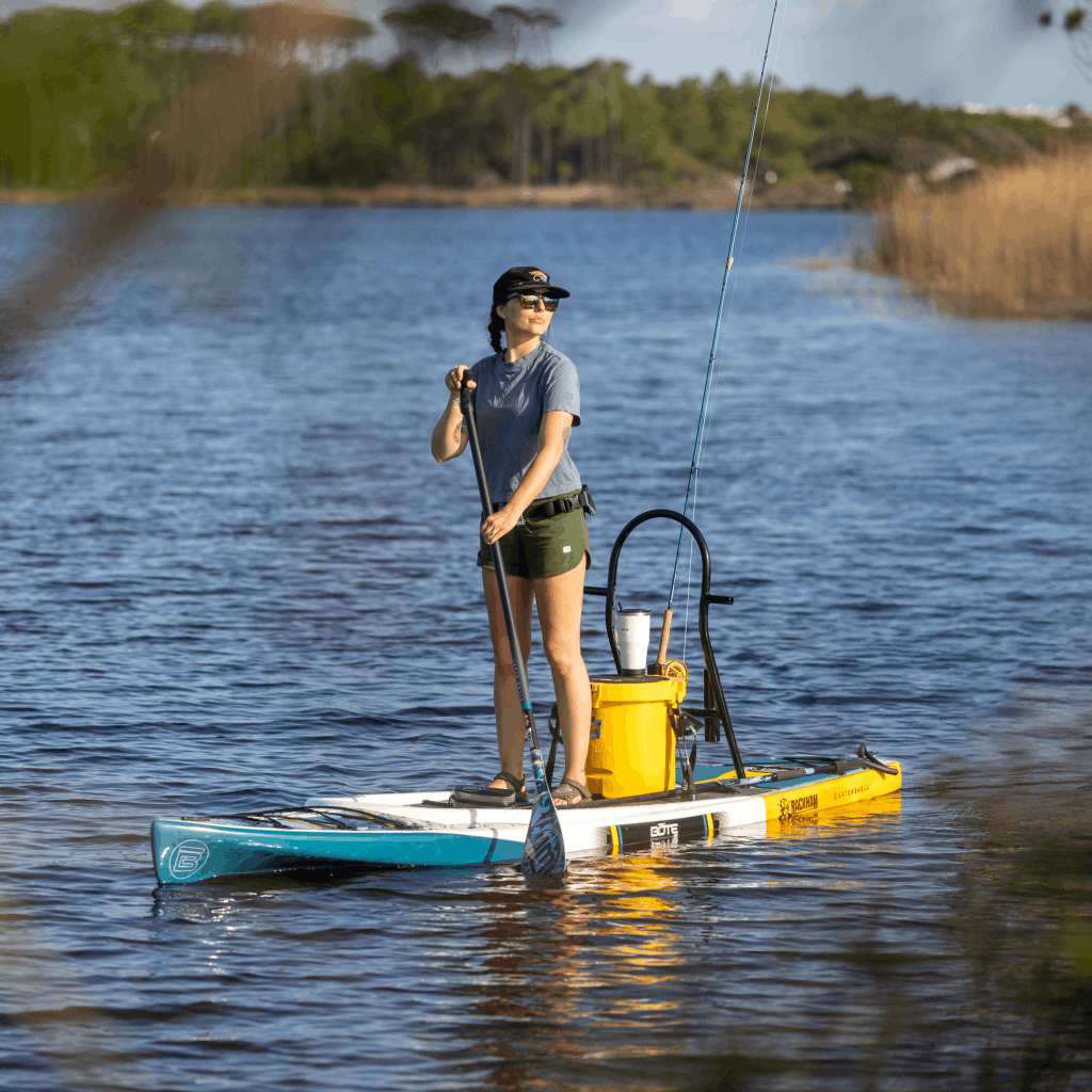 Angled view of Rackham Gatorshell paddle board with cooler and fishing gear on water.