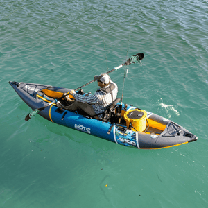 Overhead view of an angler paddling a BOTE Argo inflatable fishing kayak on green water with two fishing rods and a yellow cooler secured on deck.
