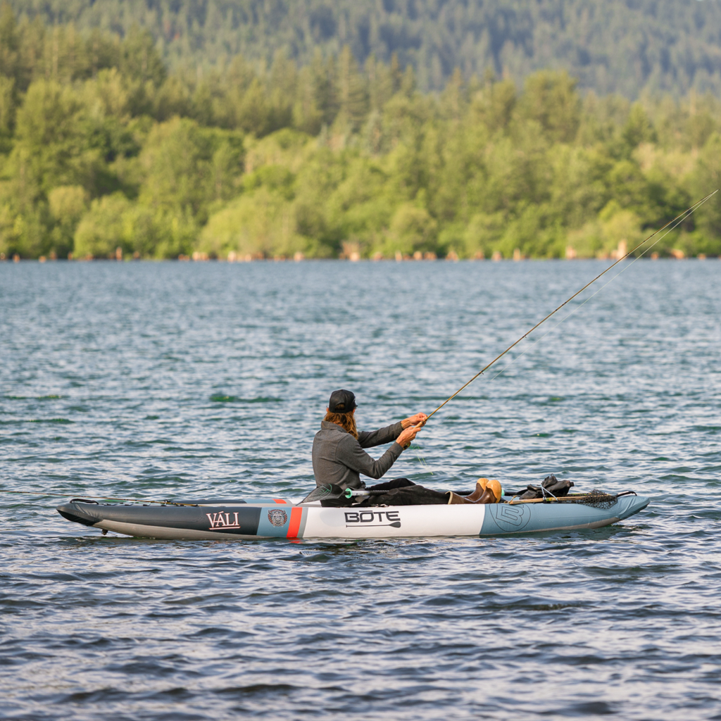 Person fishing from an inflatable kayak on a lake with trees in the background