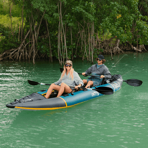 Two people paddling a BOTE Argo teal and gray tandem inflatable kayak on turquoise water through a mangrove channel.
