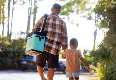 KULA Mule cooler carried by person walking with child on wooded path.