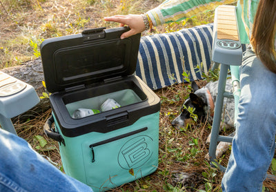 KULA Mule cooler open outdoors with drinks inside near chairs and dog.