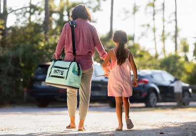 Lifestyle view of person carrying Mule Tote by shoulder strap while walking with child outdoors.