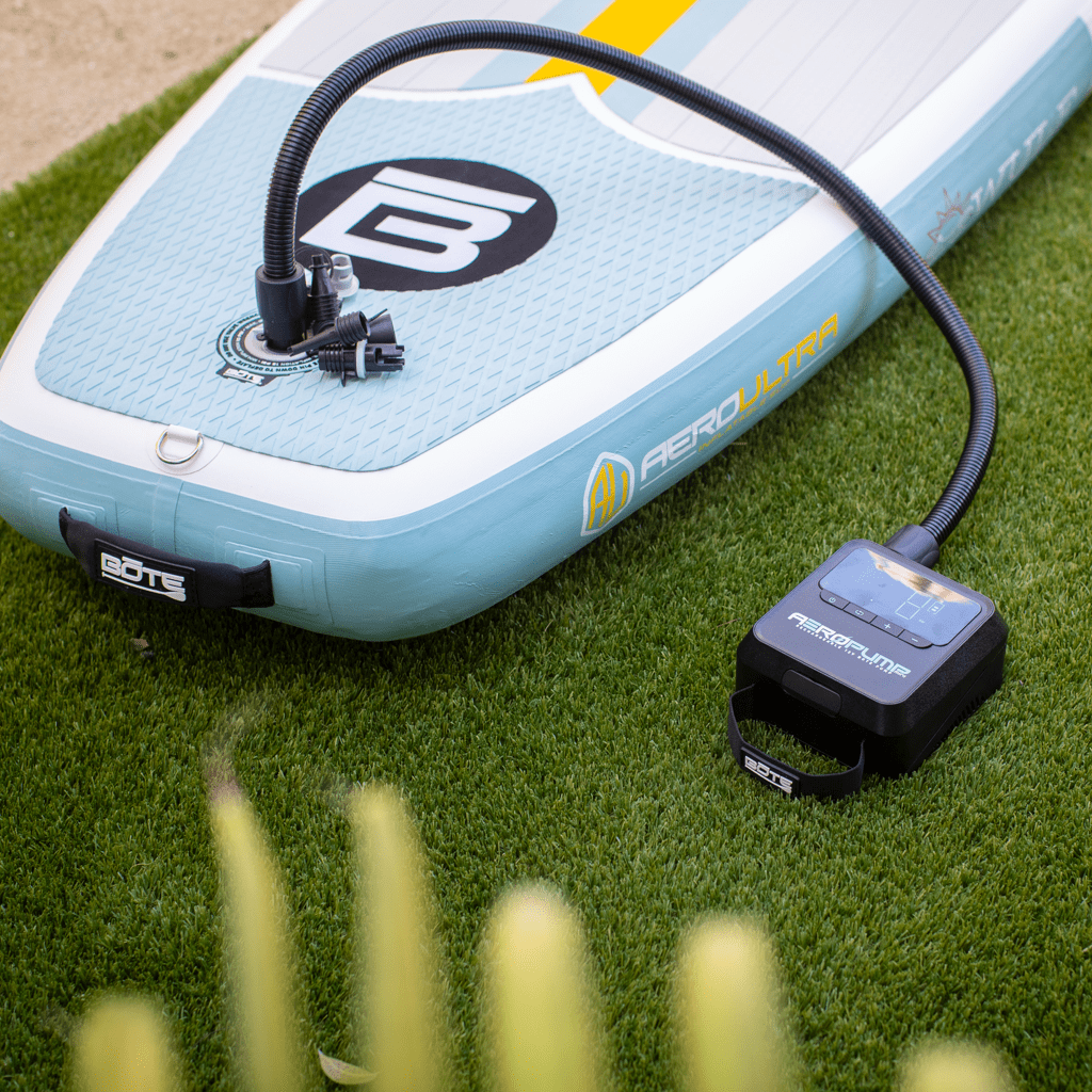 AeroPump Mini connected to inflatable board via hose, shown on green grass.