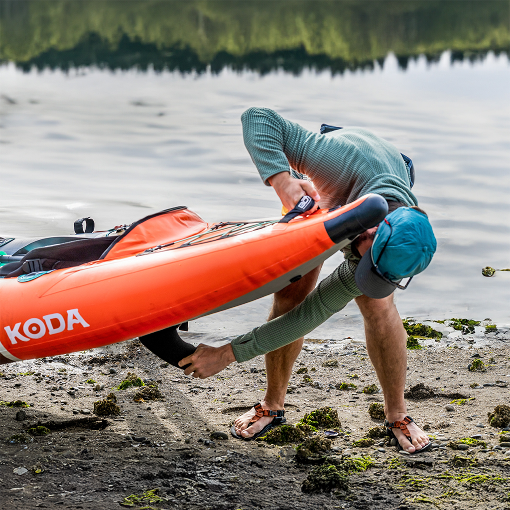 Person installing a 6" Click-In Center Fin on an orange Koda kayak by a shoreline.