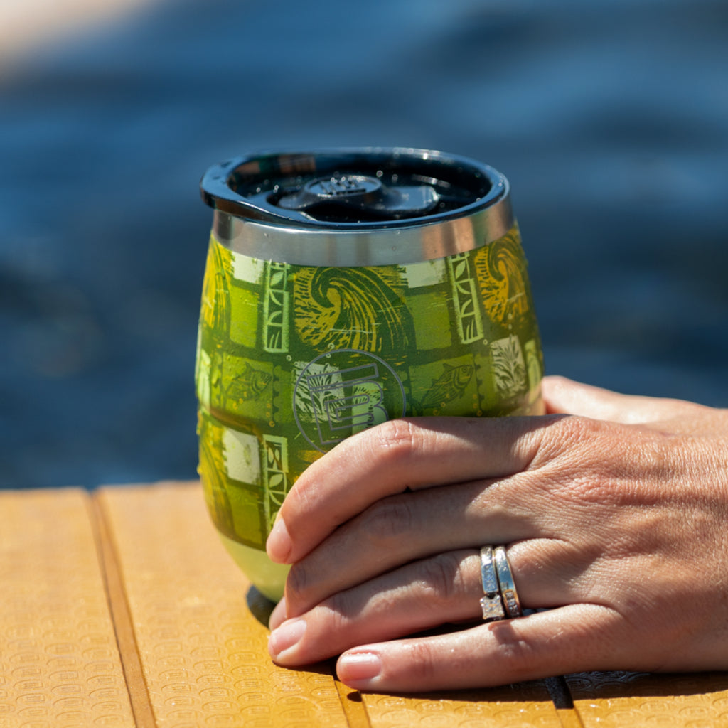 Hand holding Native Nalu stemless tumbler with lid by the water on a sunny day.
