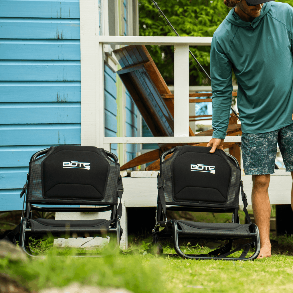 Front view of two Solis Seats on grass beside a porch with a person reaching for one.