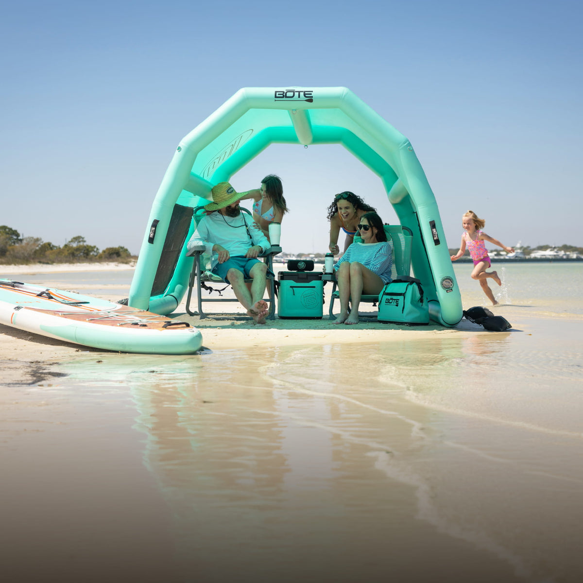 Family relaxing in chairs under the Hangout Shade inflatable beach shelter on a sunny sandbar.