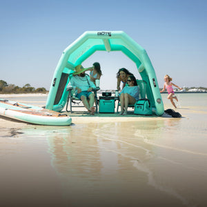 Family relaxing in chairs under the Hangout Shade inflatable beach shelter on a sunny sandbar.