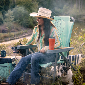 Person seated in Mule Outpost Chair outdoors with cooler and dogs nearby.