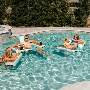 Three people relaxing on inflatable pool loungers and the Hangout Side Piece.