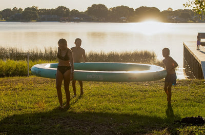 Three kids carrying a Hangout Water Hammock from shore into a lake at sunset.