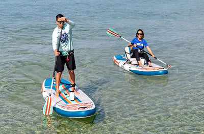Man standing and woman sitting paddling EasyRider Aero boards together.