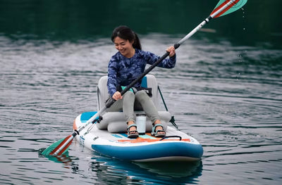 Woman smiling while paddling the EasyRider Aero on calm water.