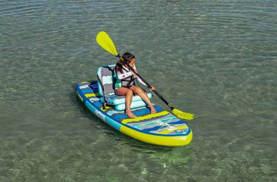 Child paddling on a Kids FlowRider Aero with seat setup over clear shallow water.