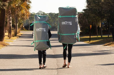 Two people walking with large BOTE travel bags for the Kids FlowRider Aero.