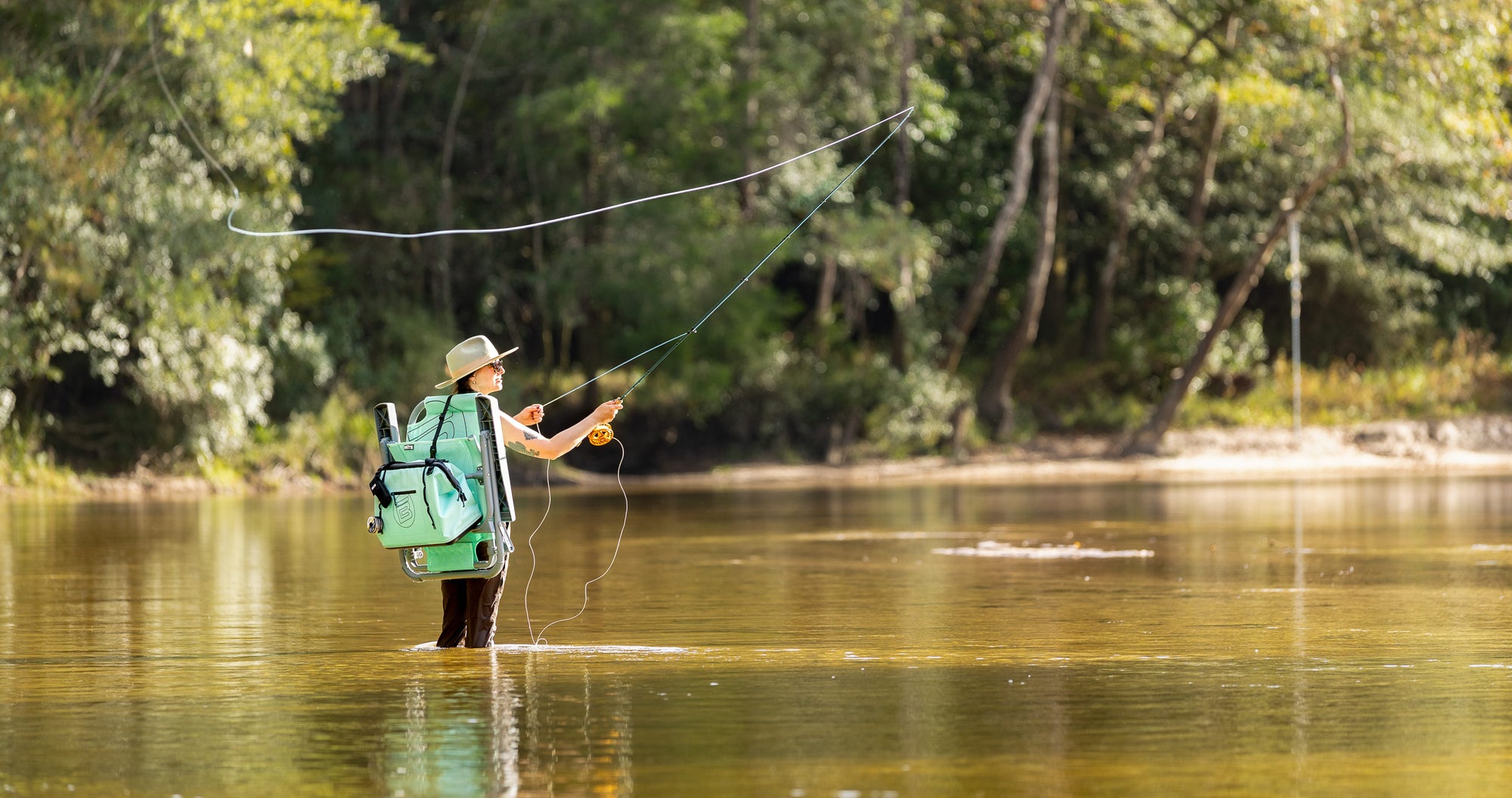 Lifestyle view of person fly fishing while wearing Mule Tote attached to chair.