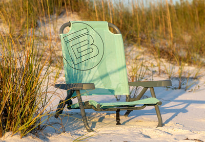 Front view of beach chair on sand with armrests and fabric backrest among dune grass.