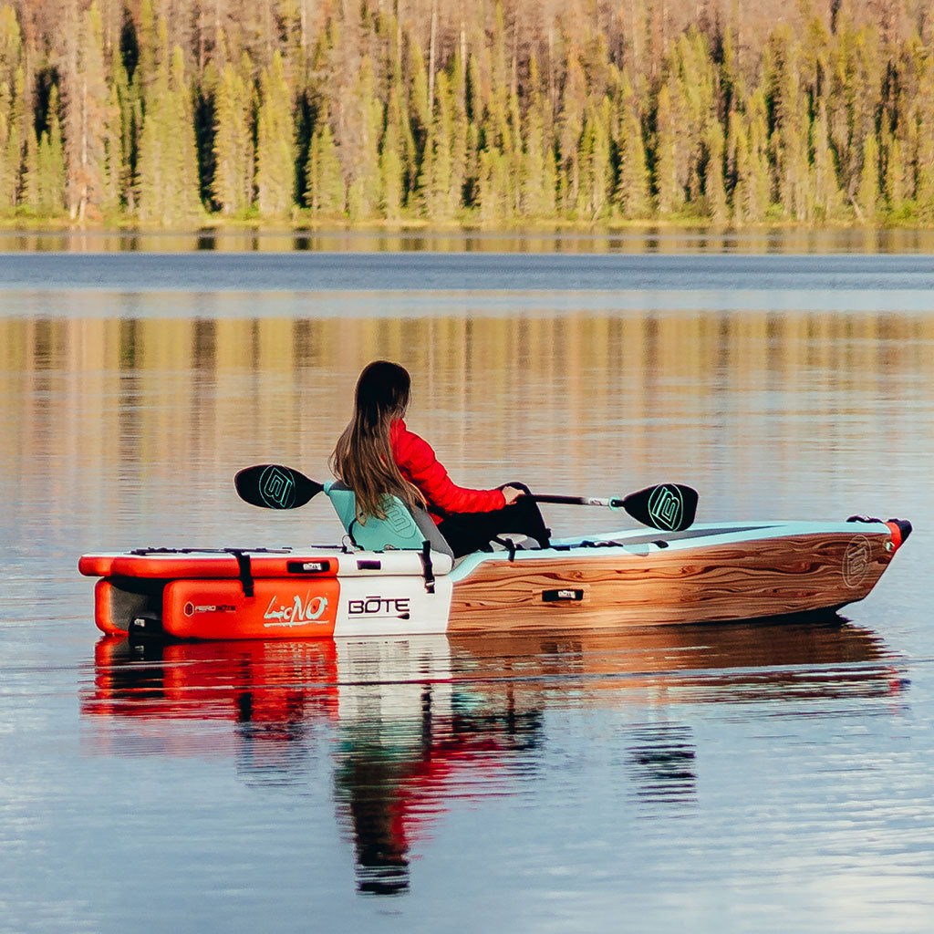 Person paddling a kayak on a calm lake with trees in the background