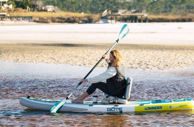 Woman kayaking on the LowRider Aero near the shore with paddle and seat setup.