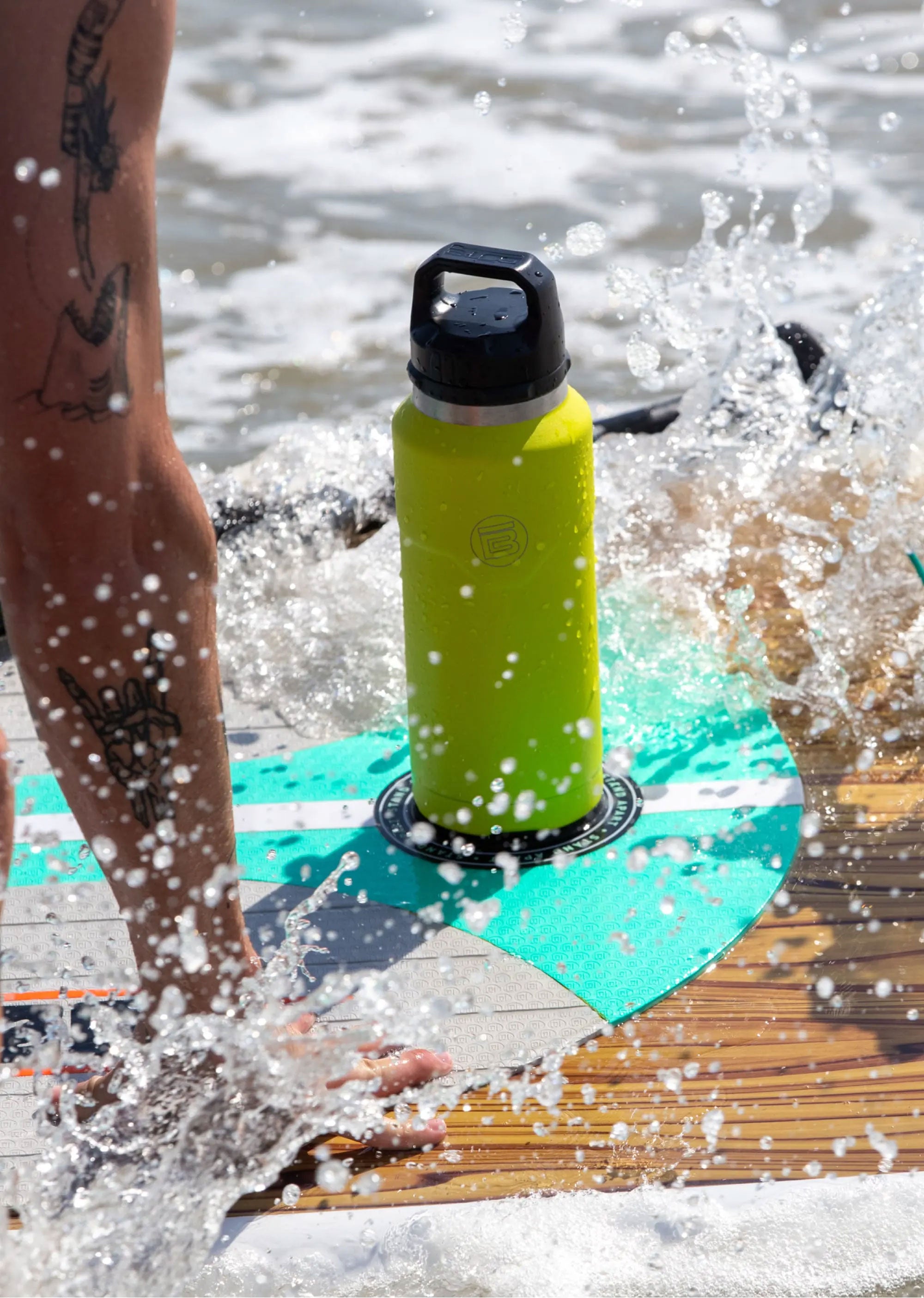 Front view of green MAGNEPOD bottle secured to a paddle board in splashing water.