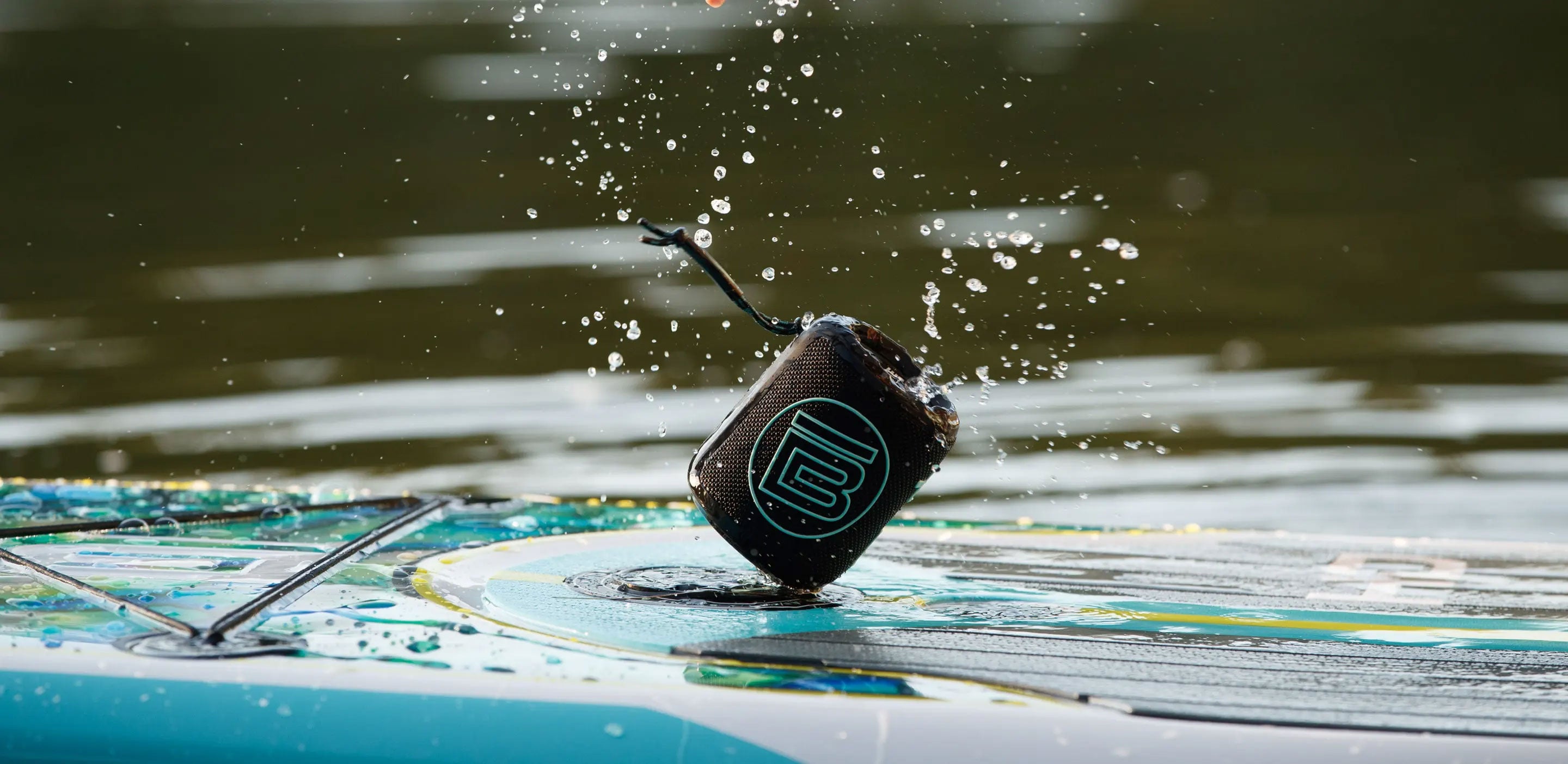 Angled view of black MAGNEPOD speaker attached to a wet paddle board.
