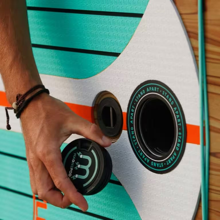 Close-up view of a hand placing a MAGNEPOD cap near a paddle board mount.