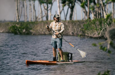 Person standing and paddling the Rackham Gatorshell APEX across calm water near mangroves.