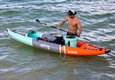 Side view of the Koda Aero Tandem with man holding a paddle, with a cooler mounted on the rear deck.