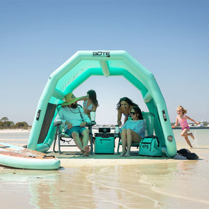 Family relaxing in chairs under the Hangout Shade inflatable beach shelter on a sunny sandbar.